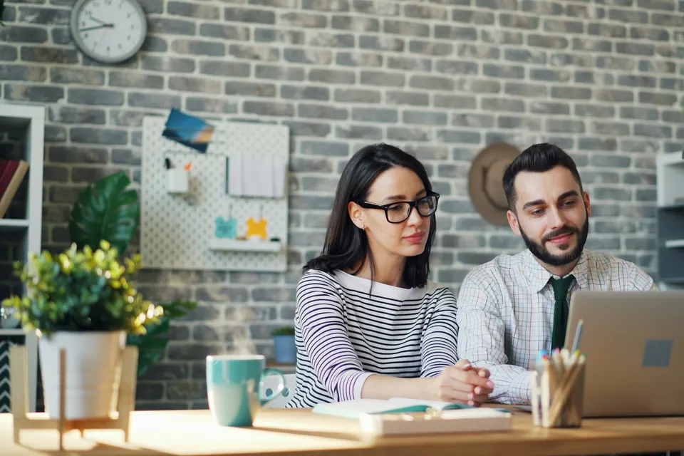 A couple sitting together at a table, looking at a laptop
