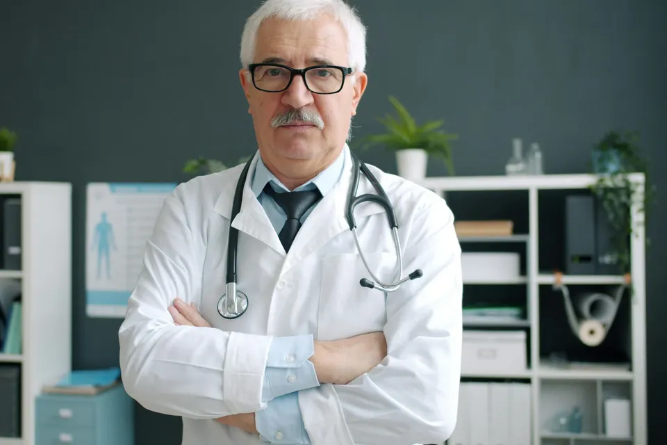 A doctor in a white coat with a stethoscope standing in his clinic