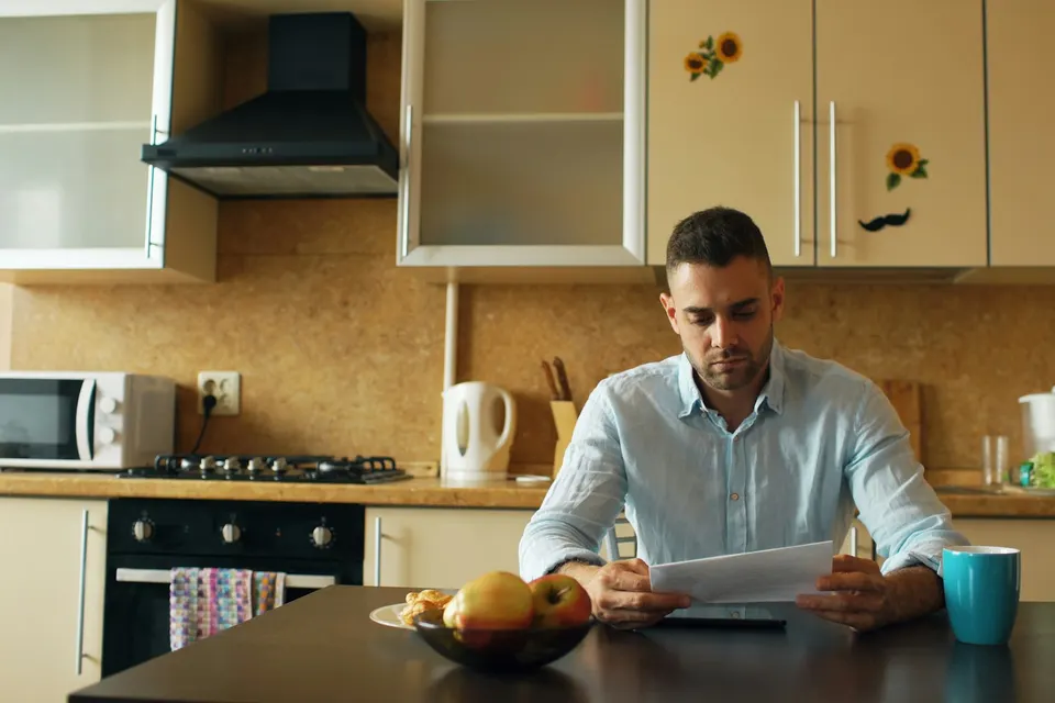 A man at his kitchen table with a cup of coffee, reading a letter
