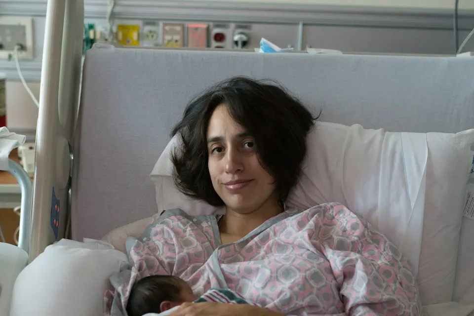 A mother resting in a hospital bed with her sleeping newborn on her chest