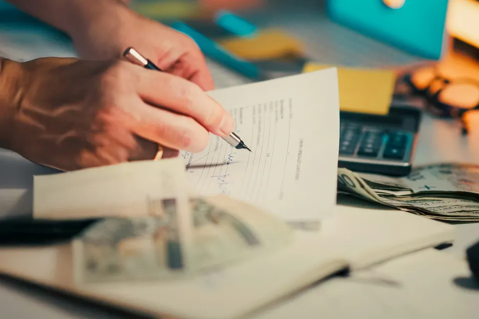 Close-up of a hand signing a document on a desk next to a calculator