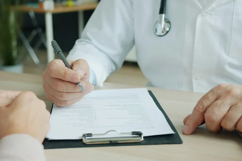 A doctor in a white coat writing on a patient's chart on a clipboard