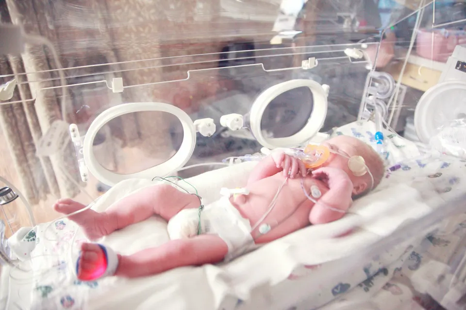 A premature baby sleeping in a hospital incubator with monitor wires attached