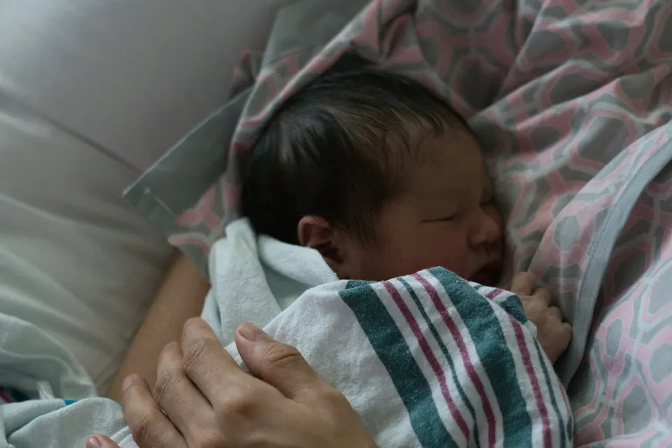 A newborn baby sleeping, wrapped in a striped hospital blanket in a parent's arms
