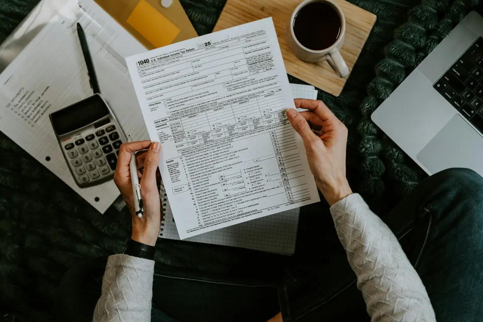 Hands holding paperwork next to a calculator, a laptop and a cup of coffee