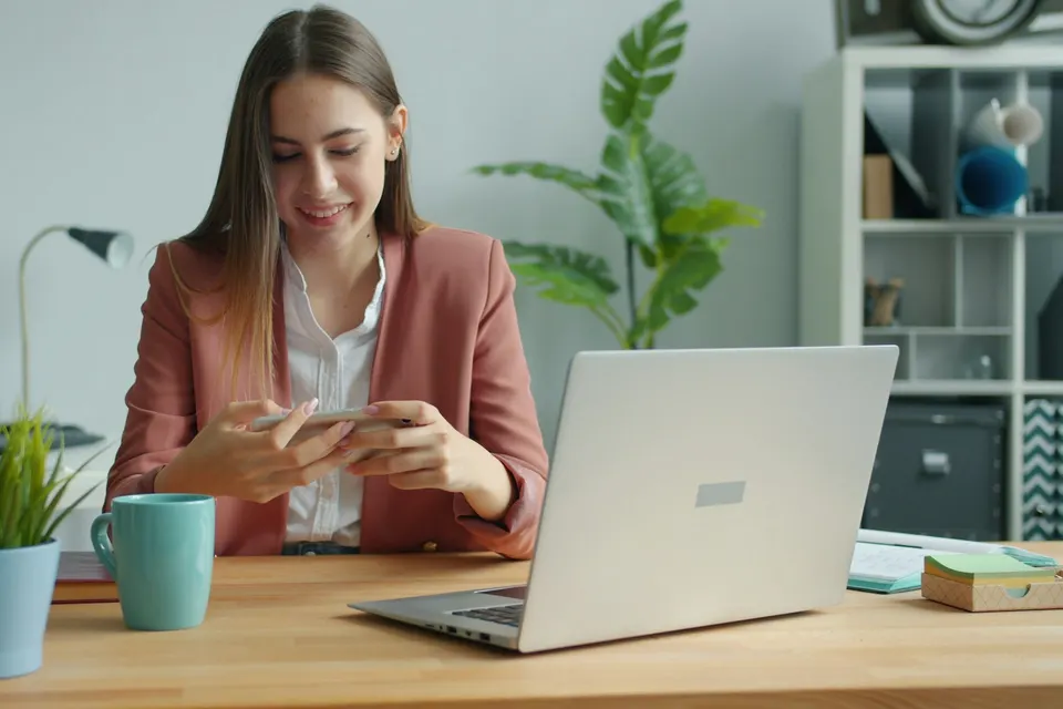 Woman at a desk with a laptop, comparing plans on her phone